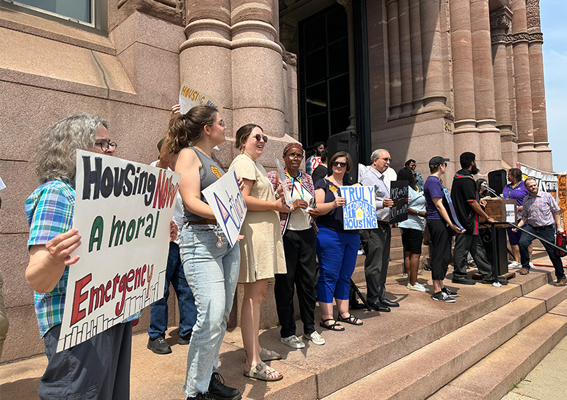 Group holding signs advocating for affordable housing on building steps