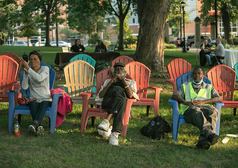 Colorful lawn chairs lined in rows on the grass with people seated.